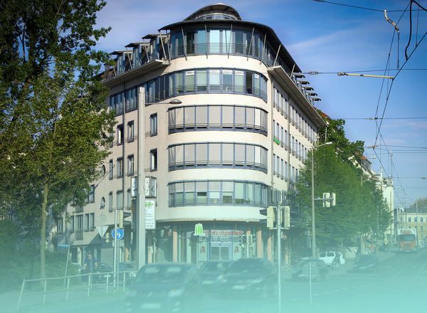 Modernes, mehrstöckiges Eckgebäude mit abgerundeter Glasfassade und Balkonen in städtischer Umgebung mit Straßenbahn und Bäumen