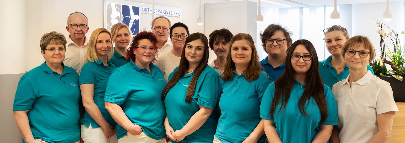 Großes Praxisteam mit 15 Mitarbeitern in türkisfarbenen und weißen Polo-Shirts, aufgestellt in modernen hellen Praxisräumen